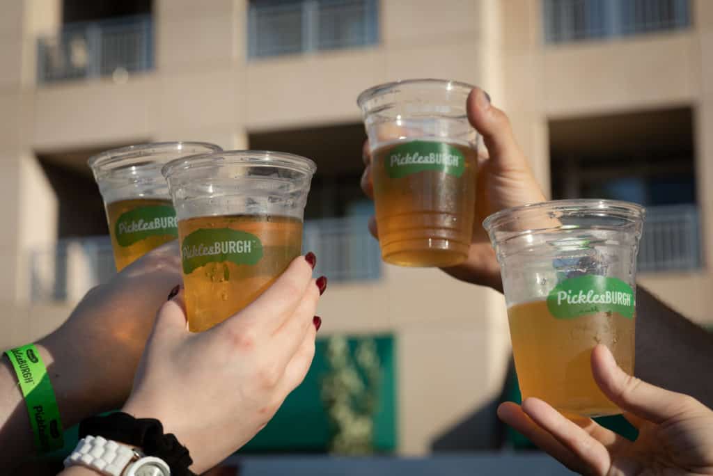 Four hands holding up plastic cups of beer at Pickelsburgh. 